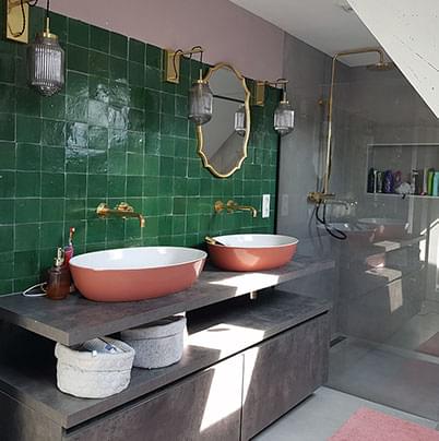 badkamer met groene tegels met dubbele wasbakken gemonteerd op een marmeren wastafel met kasten 